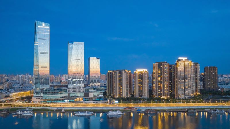 A city skyline next to a riverfront at dusk. 