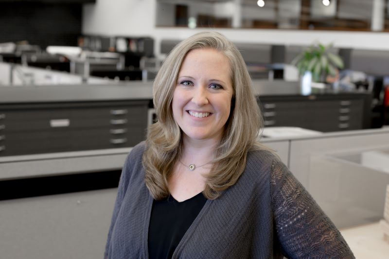 A woman standing in an office setting smiling at the camera. 