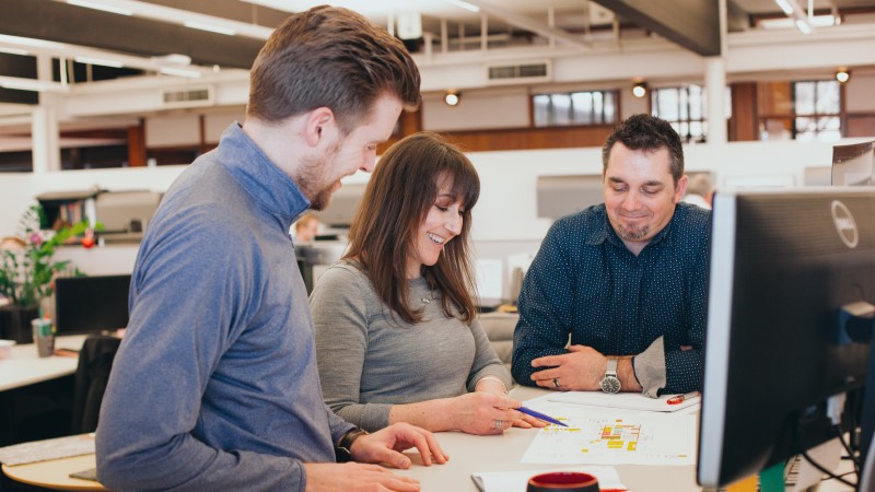 A group of architects working collaboratively at a desk, looking at plans. 